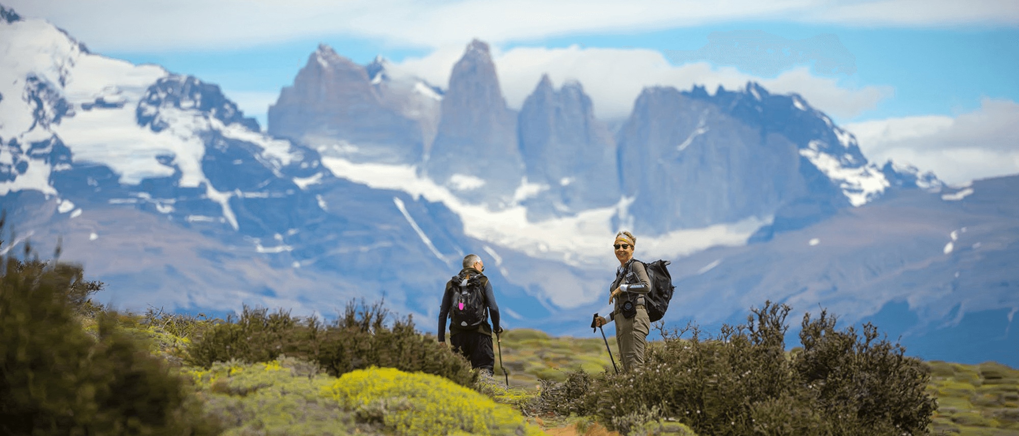 A couple on one of Tierra Patagonia's hiking adventure excursions with a breathtaking view behind them.
