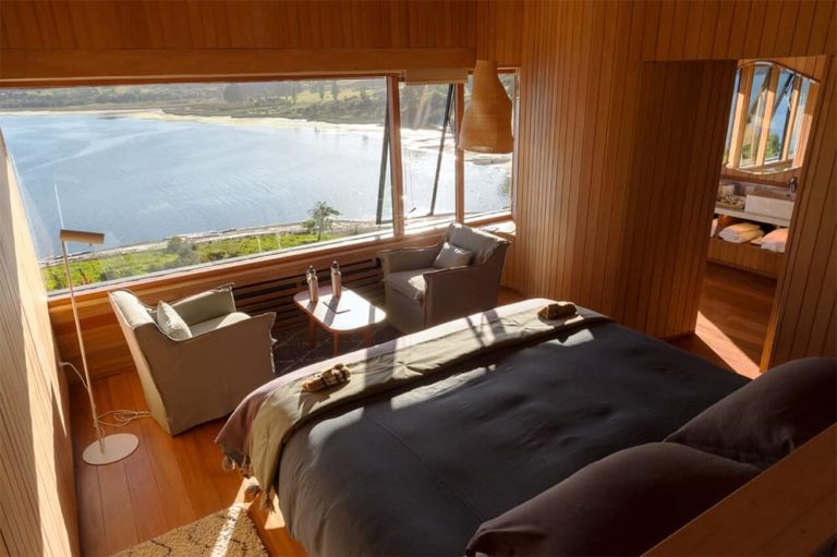 Beautiful wood covered room two chairs and a large, luxurious bed and an ocean view at Tierra Chiloe.